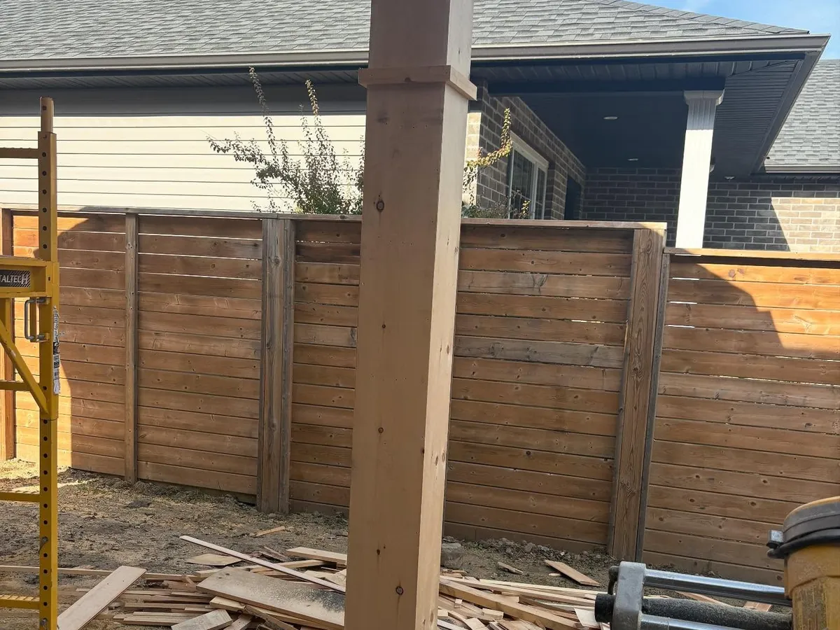 Wood fence and a new post set in a backyard.