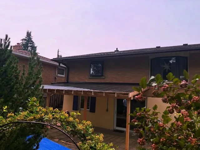 Brick house with a patio cover and black eavestroughs along the roof edge.