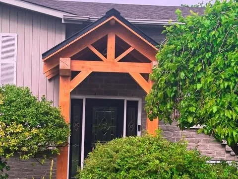 Timber portico at a house entrance under a dark roof edge.